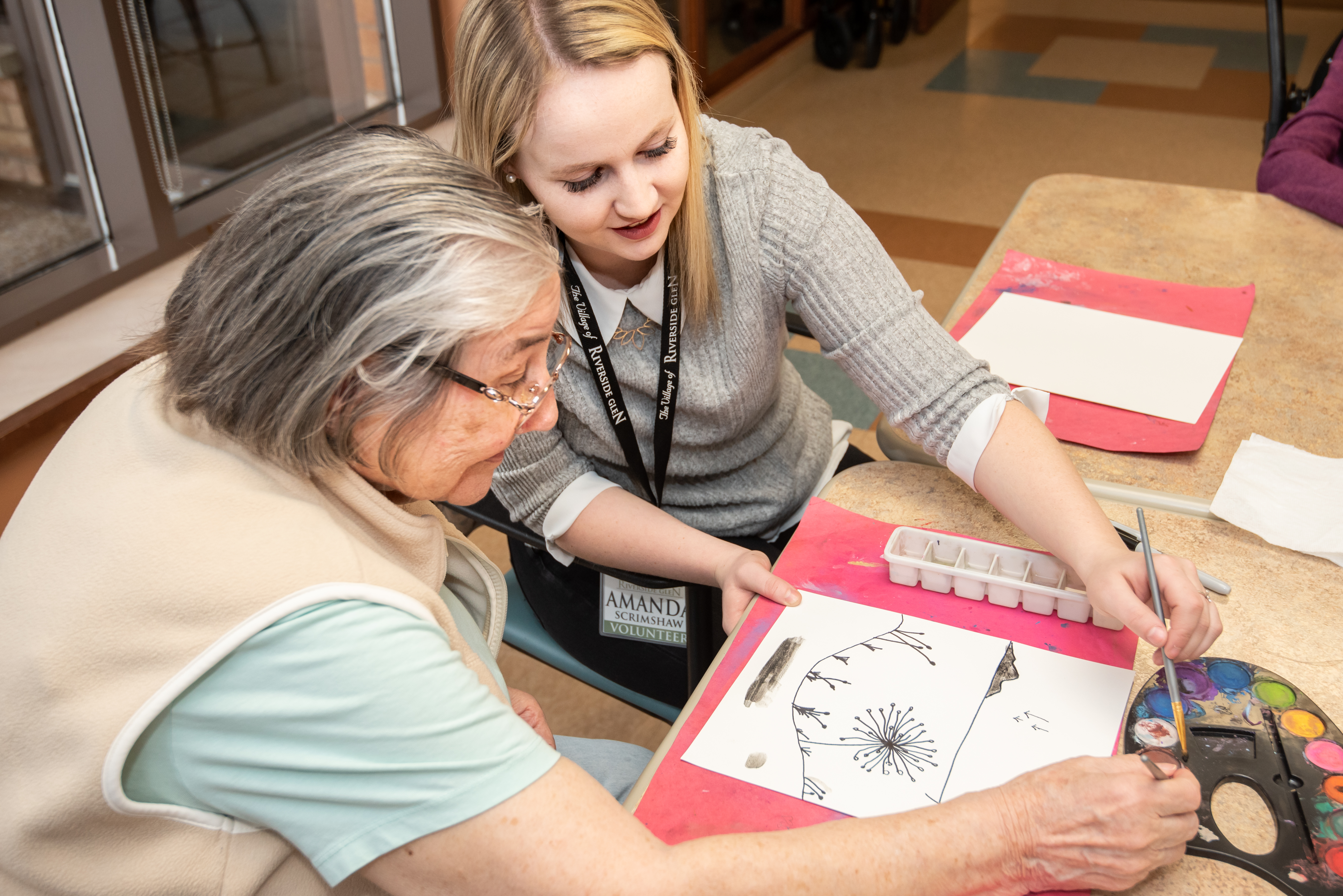 Student volunteer helping resident in a painting class