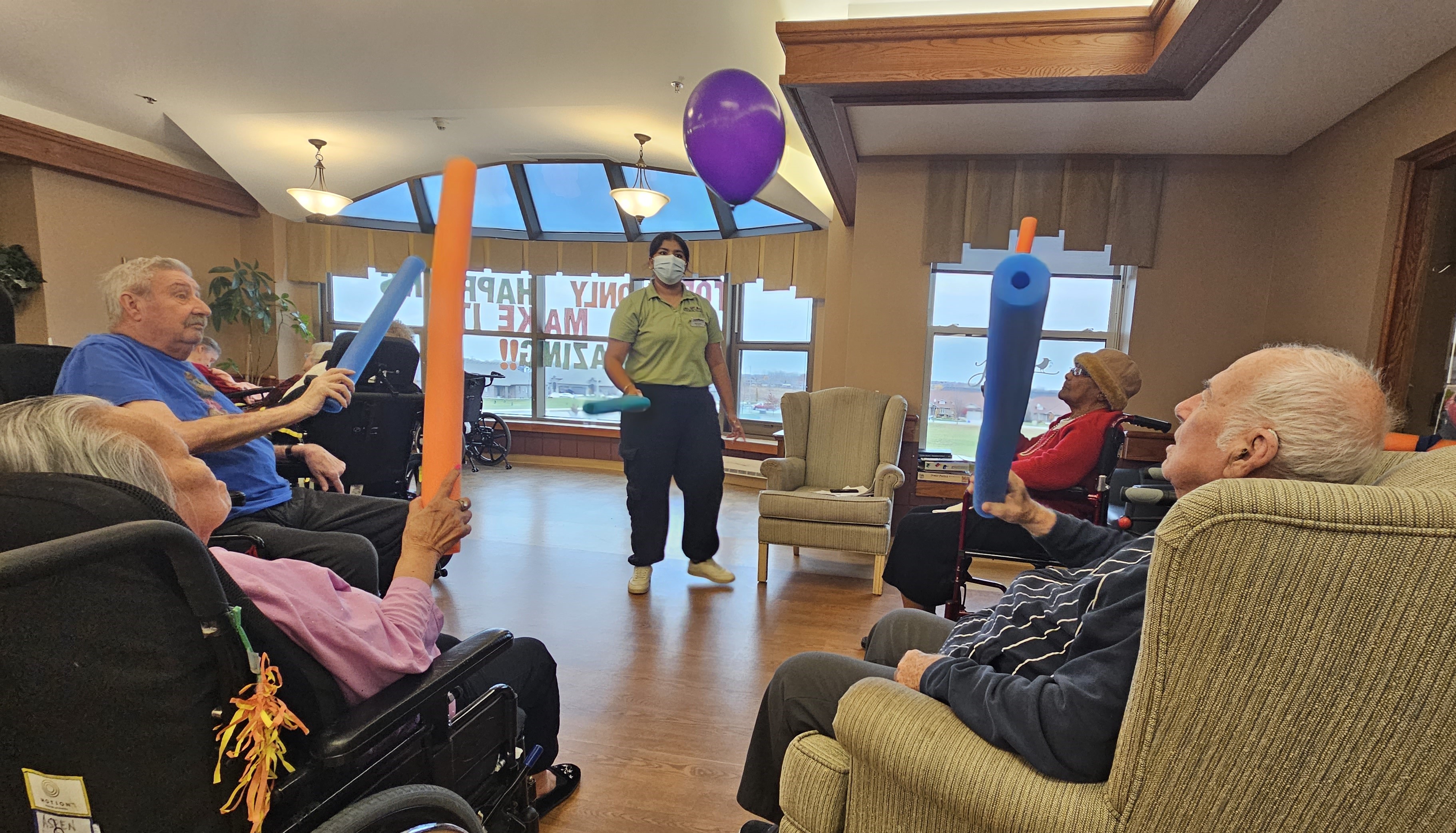 student playing balloon activity with seniors using pool noodles