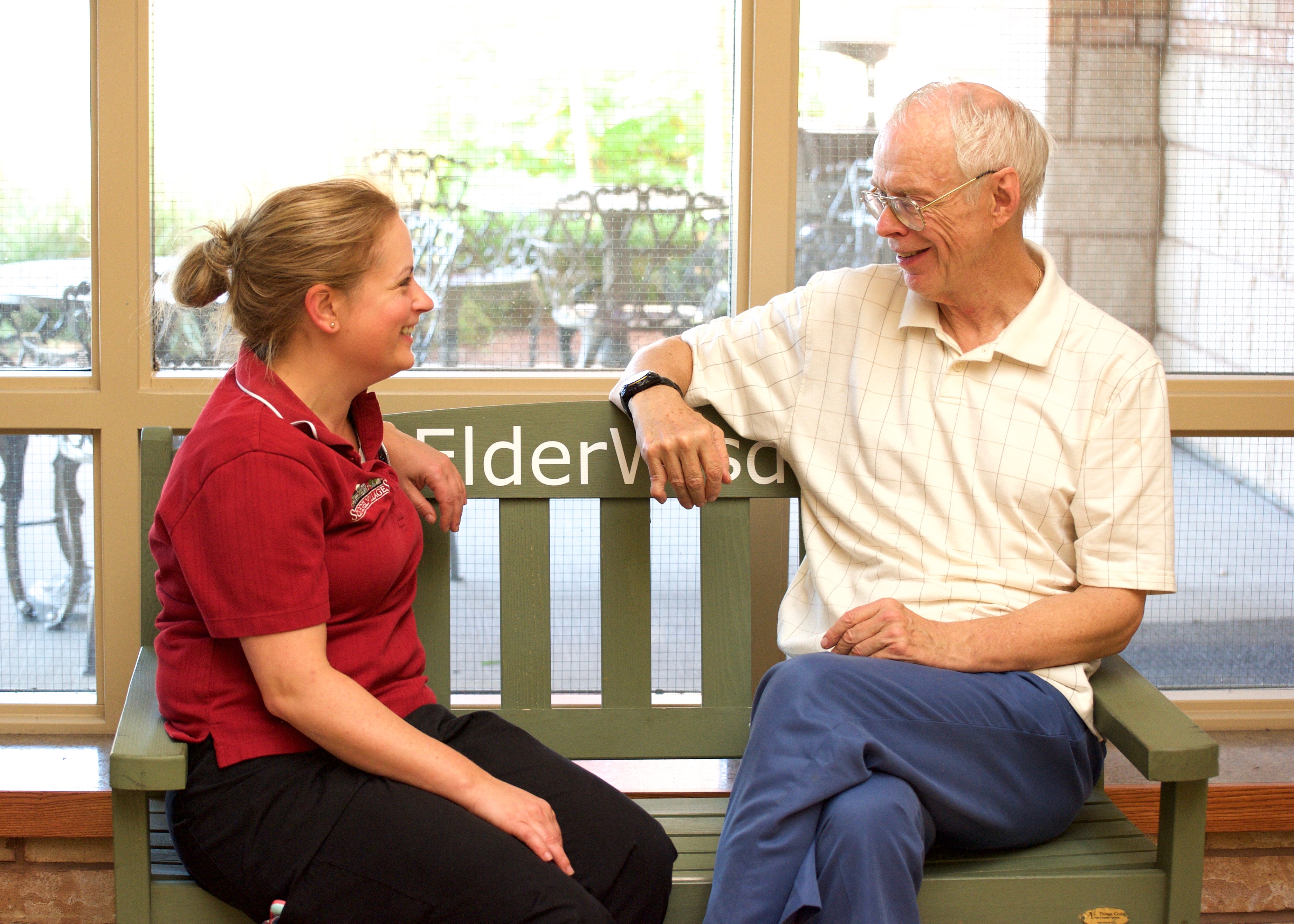 Team member and resident chatting while sitting on the #ElderWisdom green bench