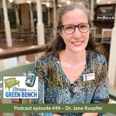 Jane Kuepfer sitting on the #ElderWisdom bench at the village promoting the Stories from the Green Bench podcast