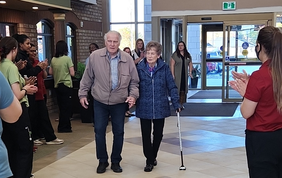 Bruce and Dorothy walk into the Village of Glendale Crossing, greeted by team members.