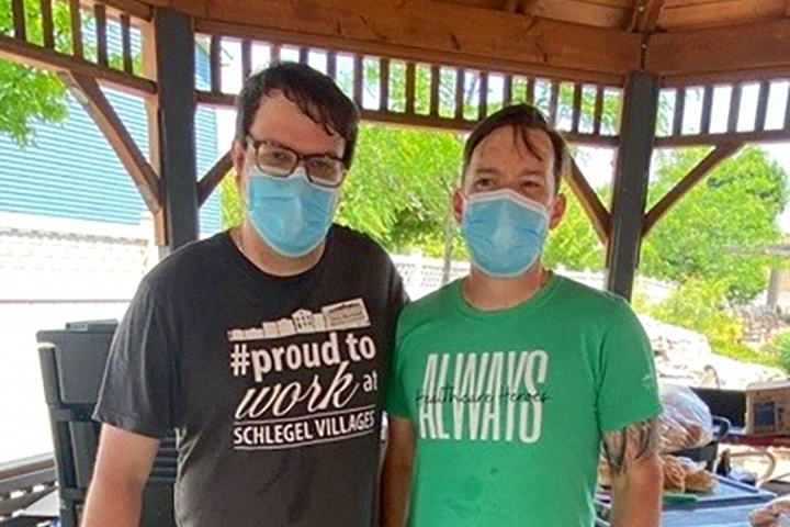 Two men pose for a photo - one shirt reads '#ProudToWorkAt Schlegel Villages' and the other reads 'Healthcare Heroes, Always'