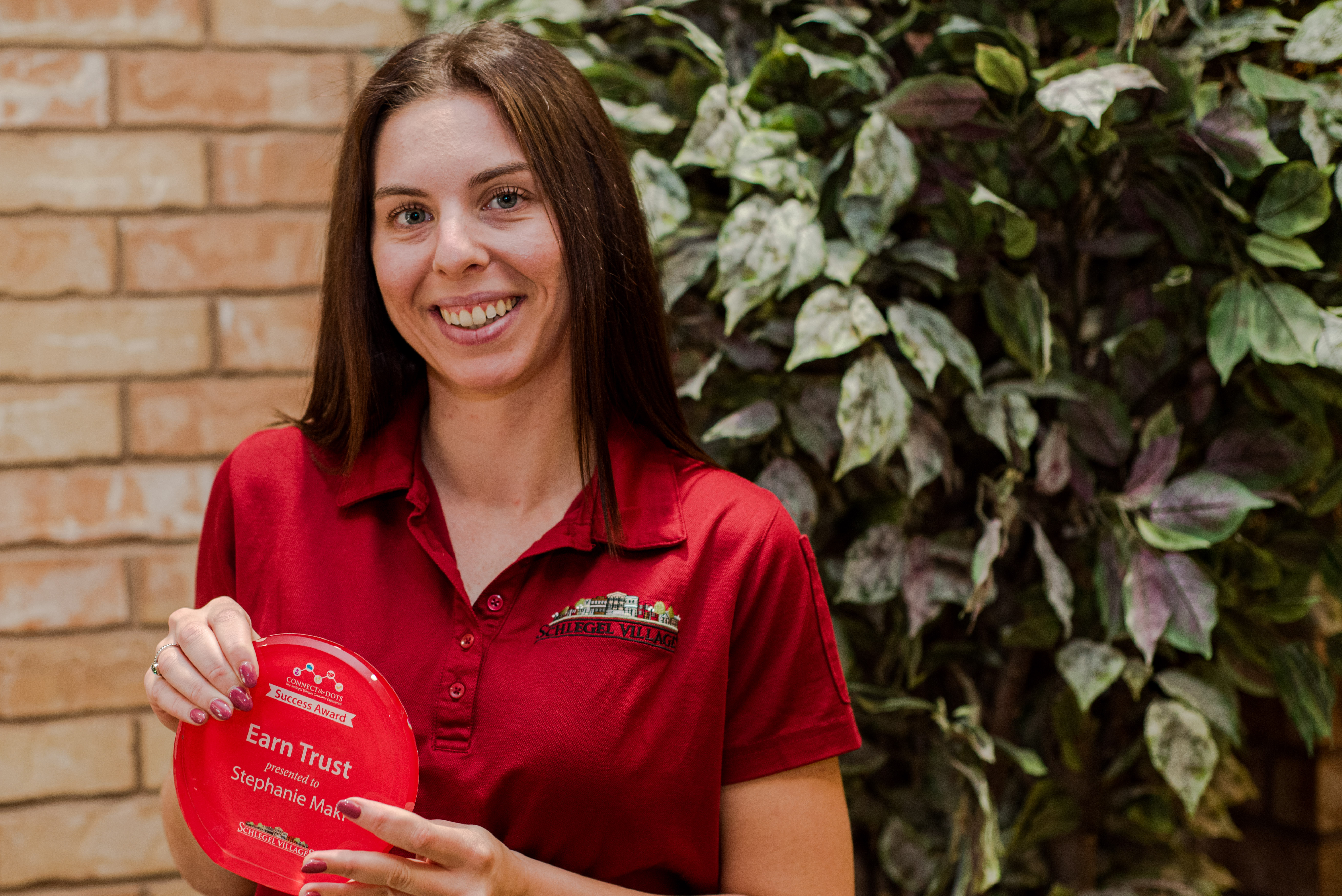 Stephanie stands smiling broadly, displaying the Success Award she received for her ability to "Earn Trust".