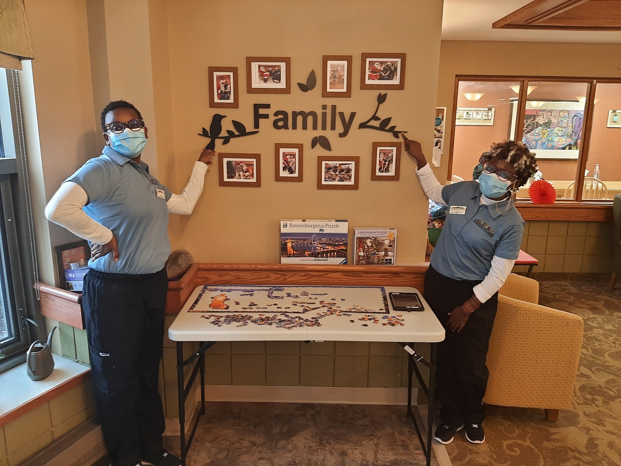 Grace and Joy stand at a wall adorned with photos and the word family. 