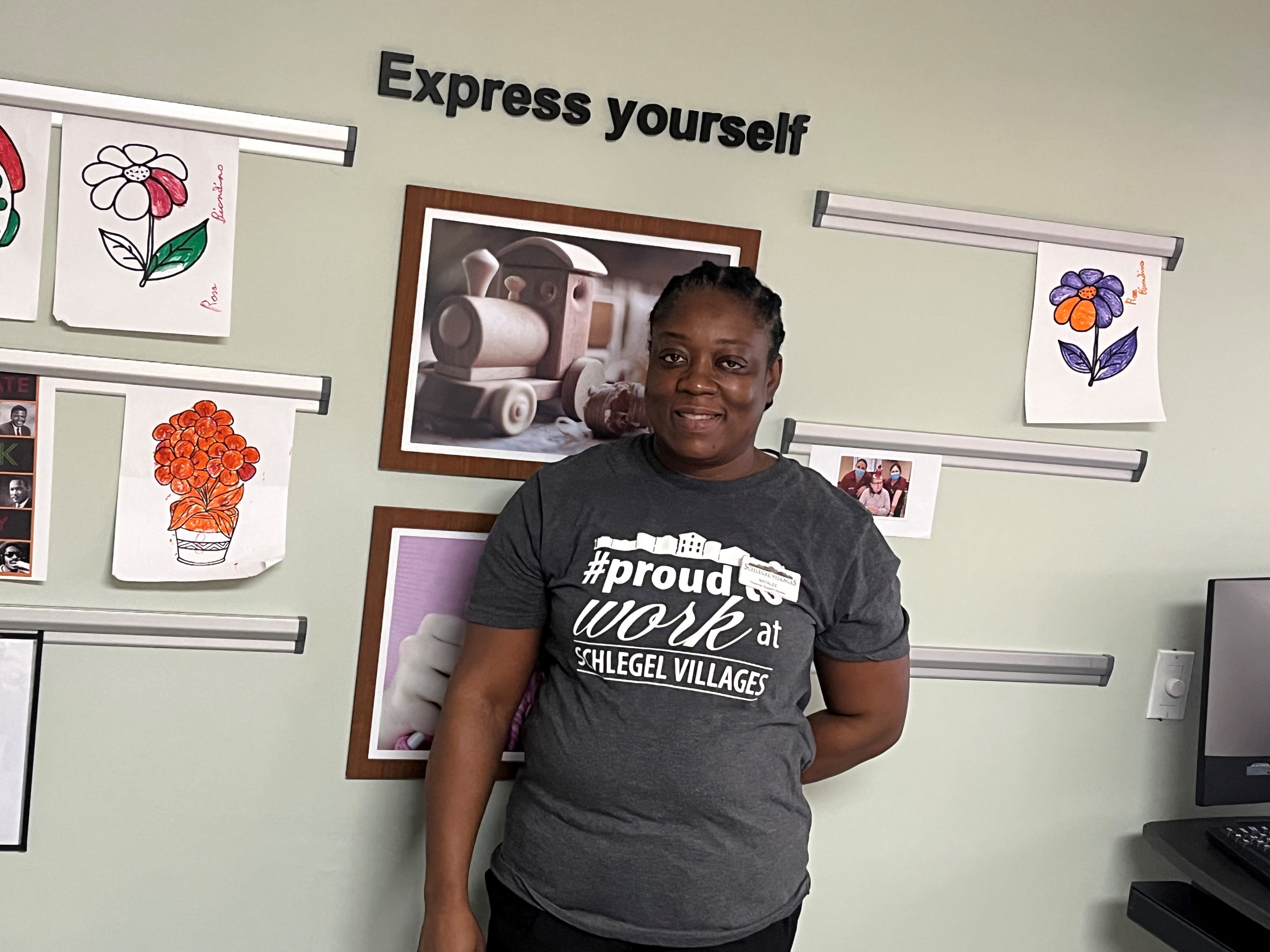 Natalee stands with a smile in her T-shirt that say she proud to work at Schlegel Villages.