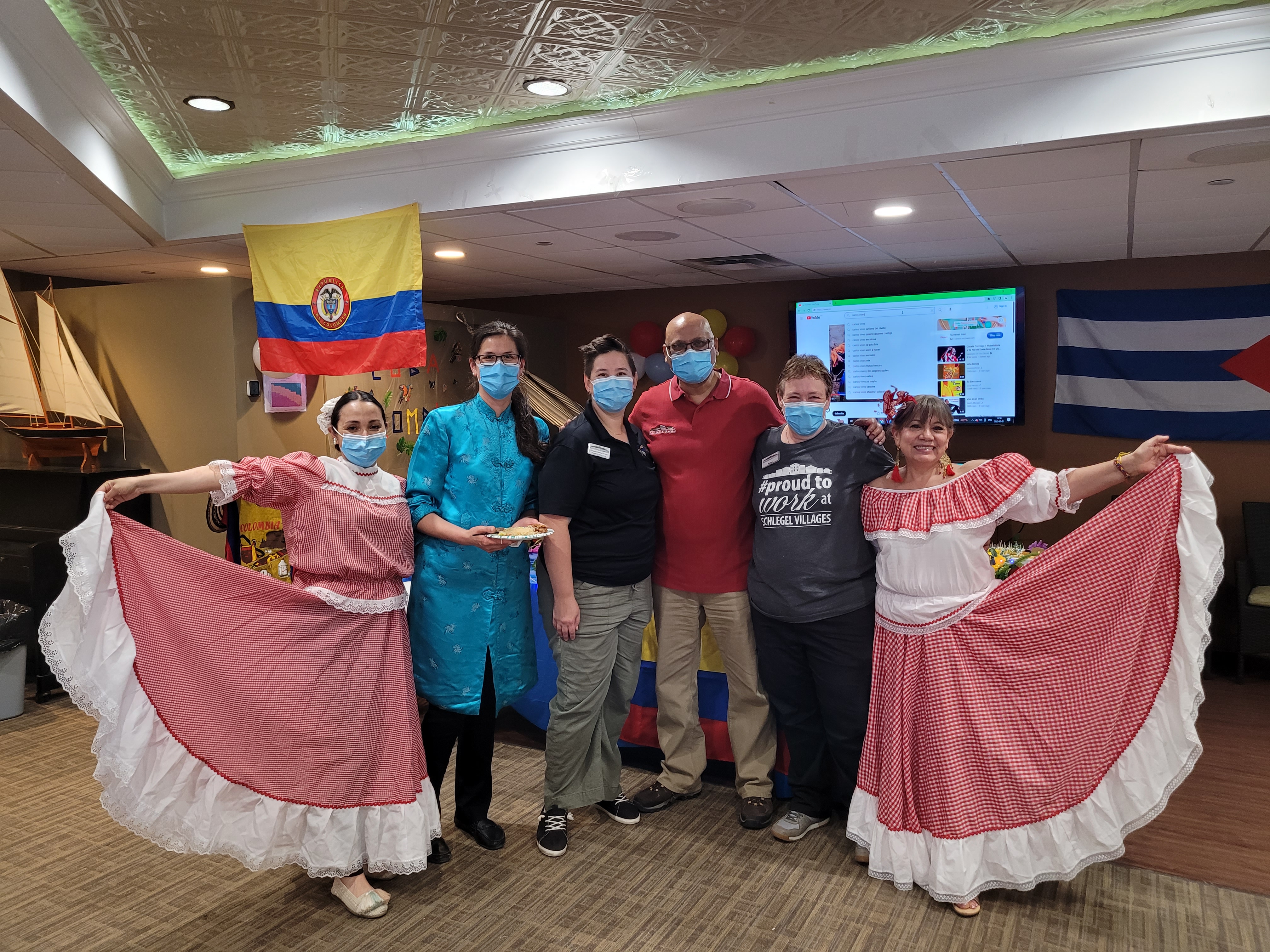 Two ladies in bright, traditional dresses flank other team members with the Columbian flag in the background.