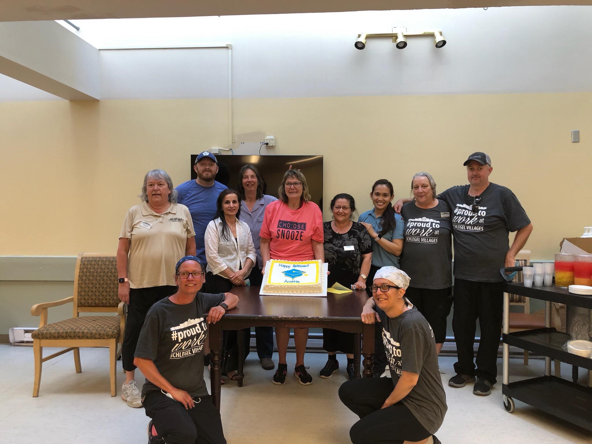 Amanda kneels at the front of a group photo with her and her team and a large cake.