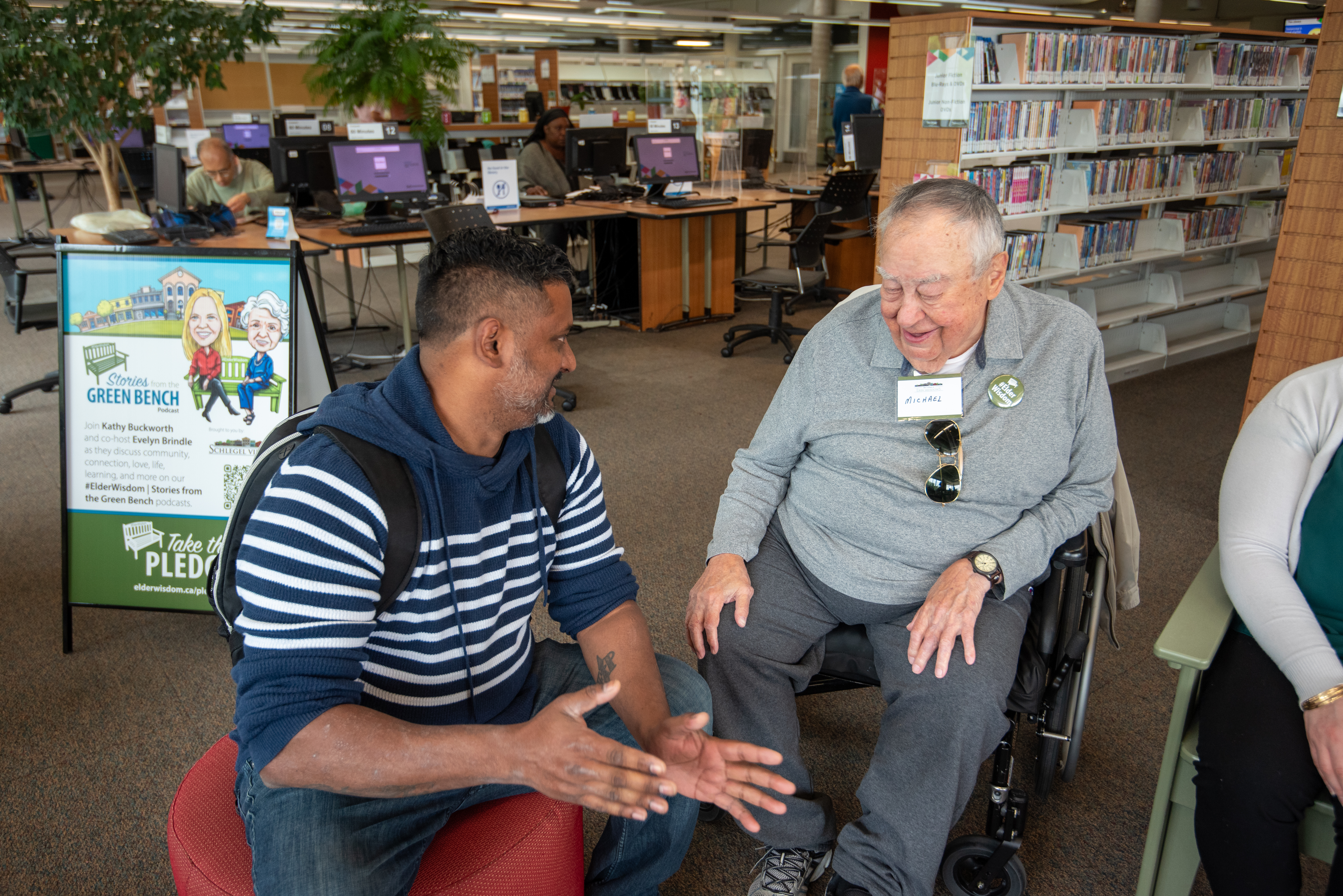 Michael sits with a visitor at the #ElderWisdom green bench in the Mississauga Library