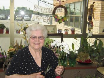 Trudy sitting in the greenhouse snipping the stem of a flower